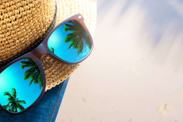 Image shows palm trees displayed in reflective sunglasses on top of a beach hat.