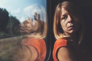 Woman looks sad as she looks out of a window of a train.