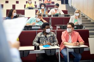 Image shows college students wearing masks in a lecture hall. 